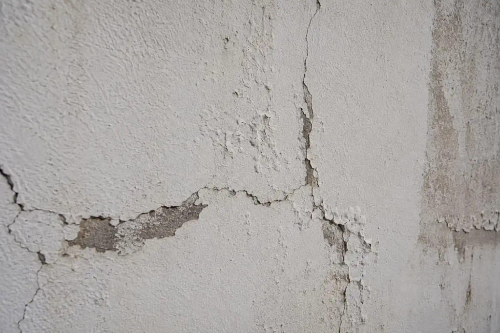 What PSI Is Safe for Washing Stucco Homes in South Florida? 2 Cracked and chipped stucco wall surface showing damage from high pressure washing